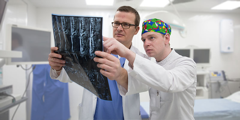 врачи онкологи клиники «Евроонко» в операционной со снимком КТ позвоночного столба